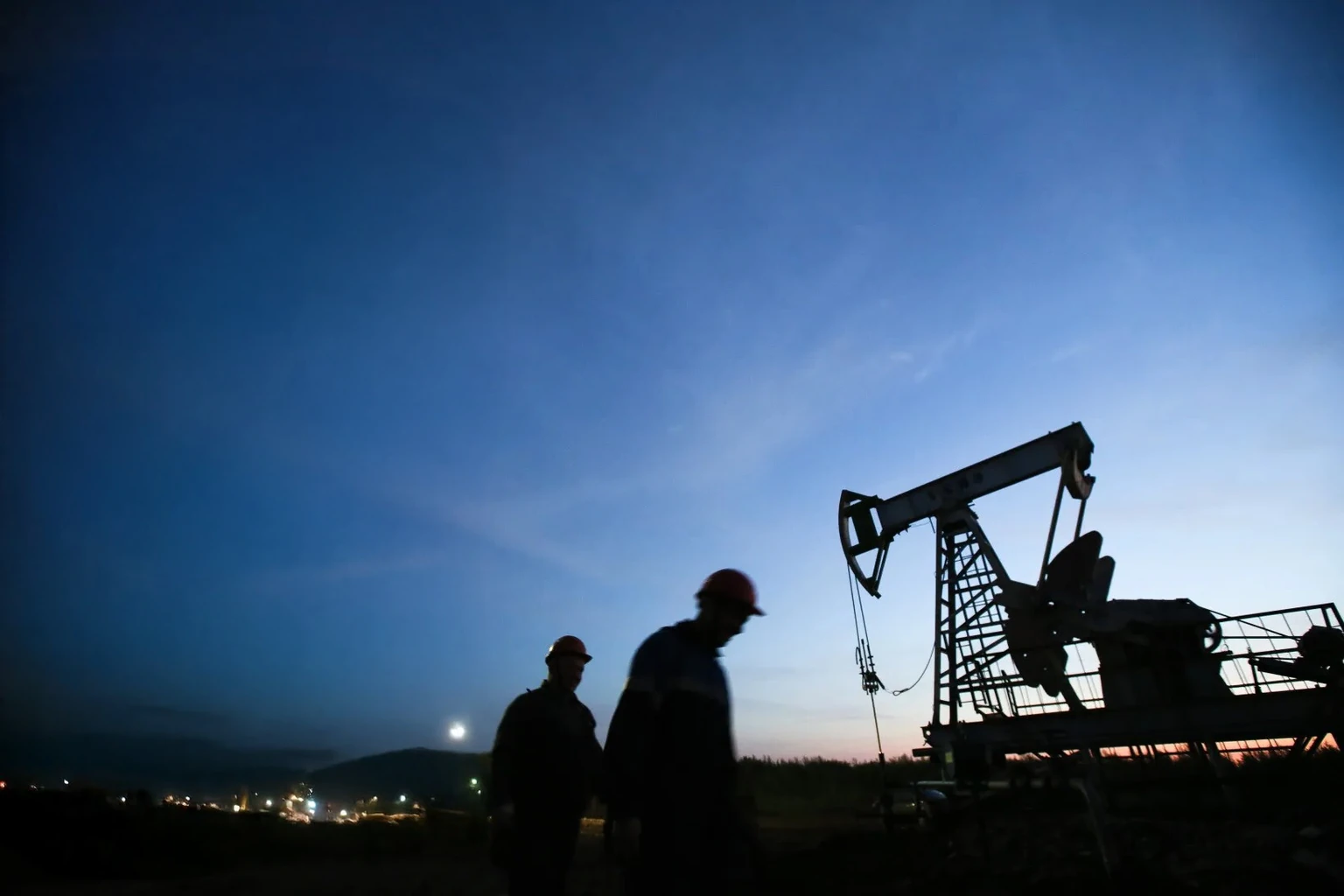 Two field workers silhouetted beside a pumpjack at dusk