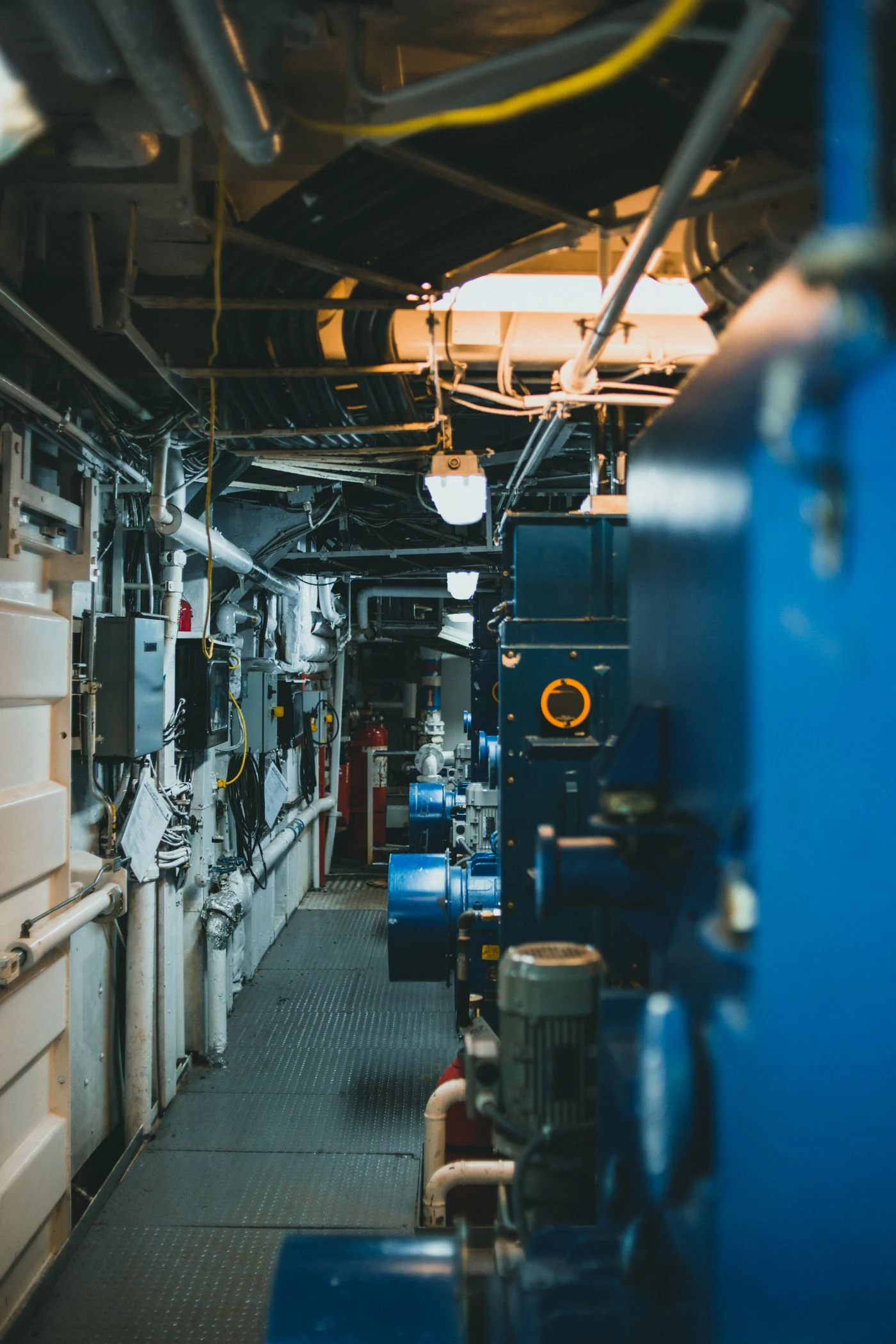 Blue industrial machinery and connected pipes inside a maintenance corridor